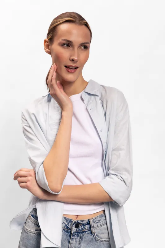 Young woman with light skin and blonde hair poses thoughtfully in casual white shirt and jeans. Studio portrait on white background with soft natural lighting for fashion concept.