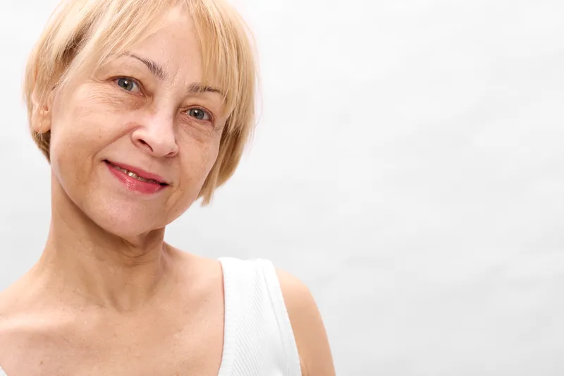 Senior woman portrait closeup with blond hair and calm smile, white studio background, healthcare clinic wellbeing, empathy and confidence for care and aging guidance now