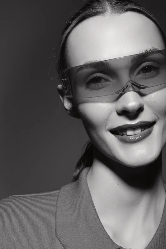Smiling Caucasian woman wearing futuristic transparent glasses in black and white portrait. Concept of technology, fashion, and modern style with light and shadow contrast.