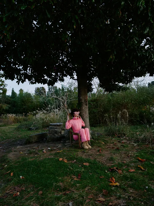 Child girl sitting under a large tree in a peaceful park, wearing a pink dress. Calm afternoon light, autumn leaves on grass, empty bench, serene outdoor scene for lifestyle, nature and quiet moments