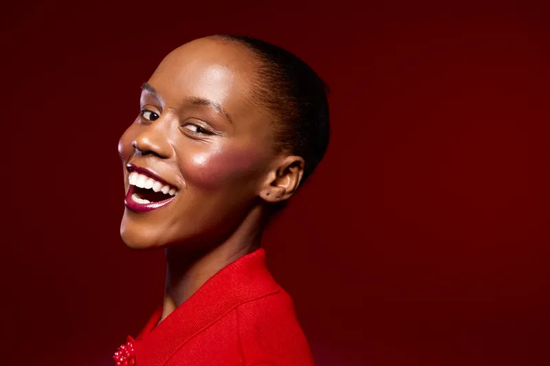 Portrait of a smiling African American woman with dark skin wearing a red outfit against a red background. Concept of beauty, confidence, fashion, and positive mood.