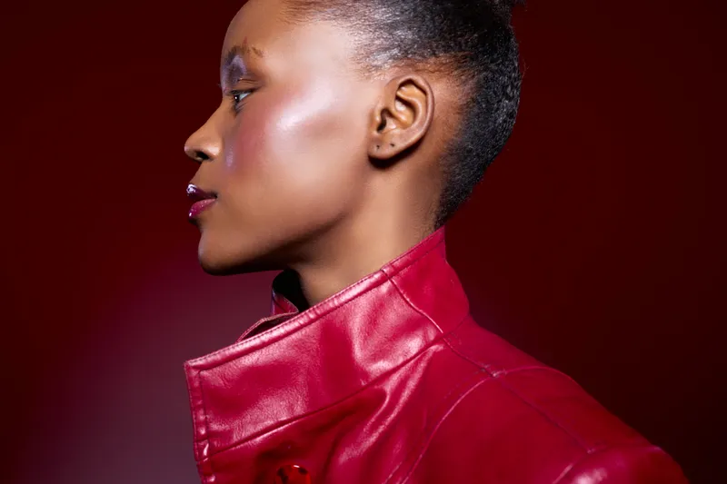 Profile of a dark skinned African woman wearing a red leather jacket against a red background. Studio portrait with dramatic lighting highlights her smooth skin and confident expression.
