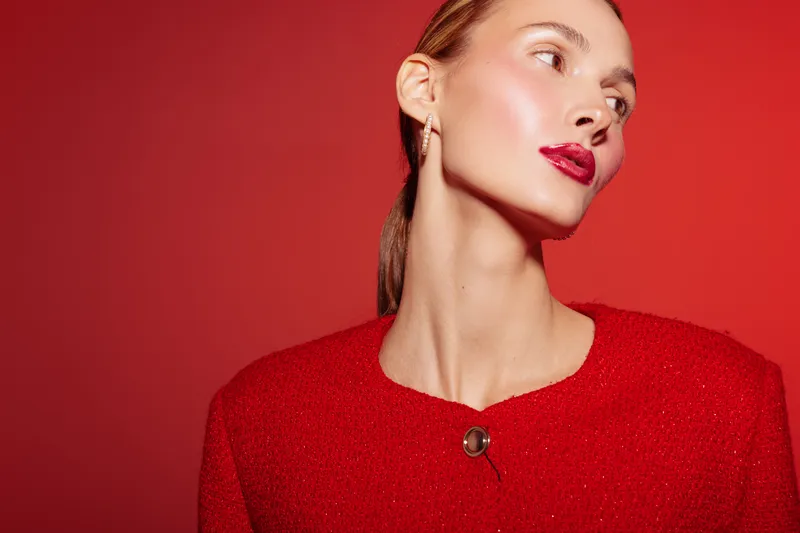 Elegant woman with red lipstick and red outfit poses against red background. Close-up portrait with smooth skin and confident expression. Concept of fashion and beauty.