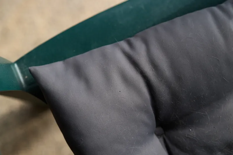 A closeup of a black cushion resting against a green metal frame on a textured surface, suggesting a cozy indoor setting and everyday comfort. The scene focuses on soft fabric, muted tones, and a