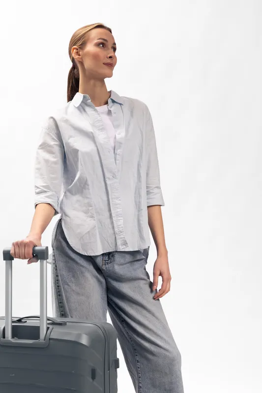 Young woman traveler with suitcase looks aside in casual clothes. Concept of tourism, journey, and travel planning with luggage for vacation or business trip.