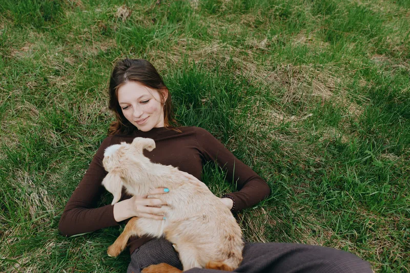Relaxed woman lying on grass outdoors, cuddling a dog, capturing a wholesome lifestyle moment with a gentle pet connection under soft sunlight in a green field.