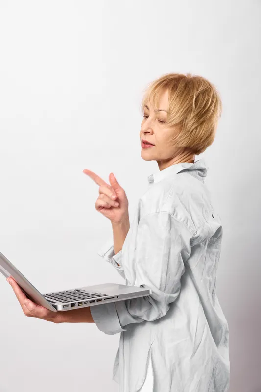Woman doctor in laboratory coat holds laptop, tense and frustrated, pointing gesture, isolated on white background, concept of stress and workplace pressure