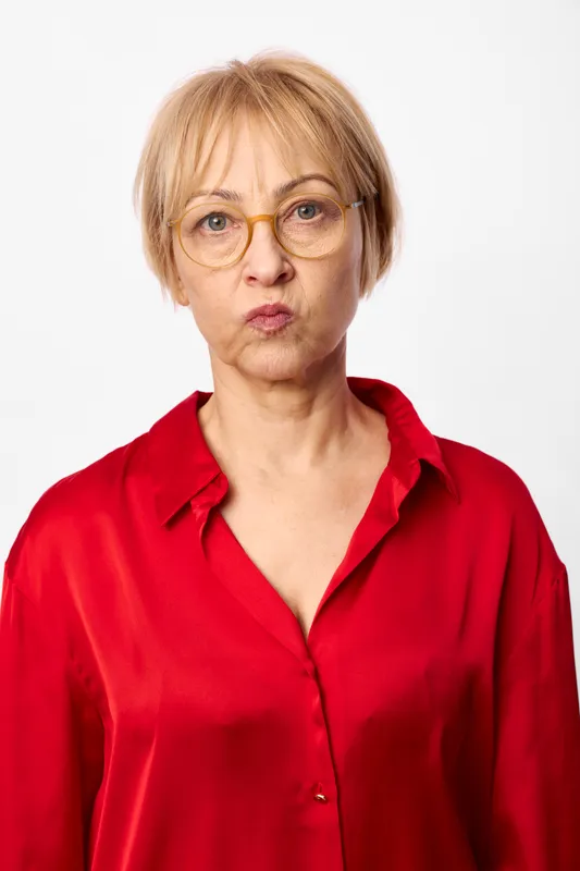 Senior woman portrait with glasses, red blouse, studio closeup face, expression, soft even light, plain white background, calm neutral pose