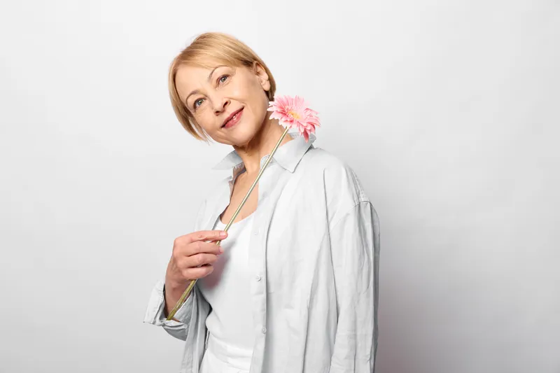 Woman, flower, smiling, white, background, studio, portrait, spring mood, blonde hair, holding pink blossom, soft light, clean backdrop, gentle relaxed