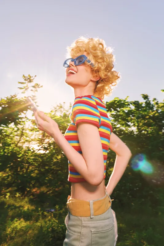 A woman in retro color outdoor fashion with sunny sunglasses and curly hair, captures a candid moment in a park, conveying lifestyle and vintage vibe in bright light.