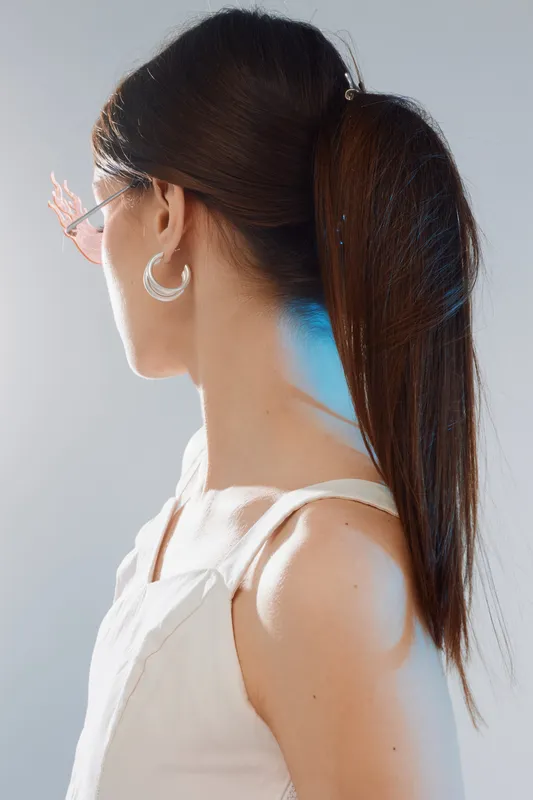 Young woman with long dark hair in a white top and hoop earrings looks to the side. Studio portrait focusing on beauty, fashion, and hairstyle concept.