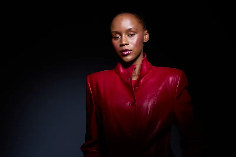 Confident dark skinned African woman wearing a red leather jacket poses against black background. Studio portrait with dramatic lighting, fashion concept highlighting elegance and style.