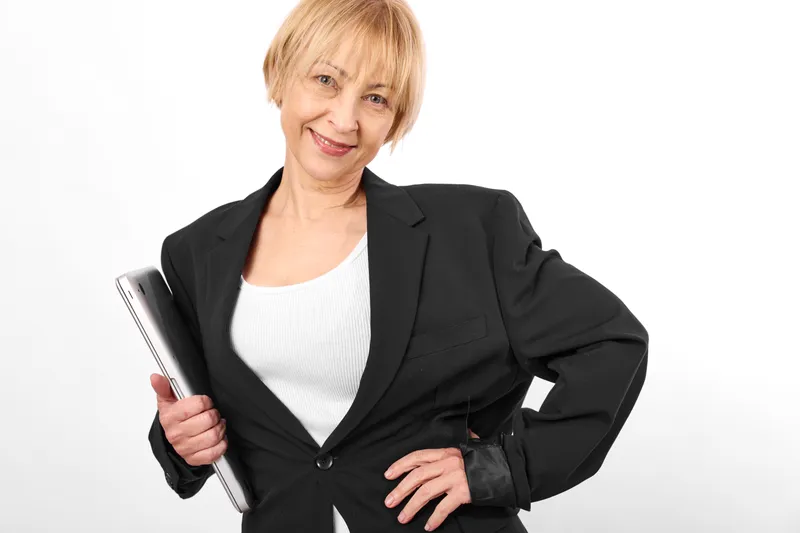 Senior woman in black blazer holding smartphone, smiling in studio white background, confident posture, short blonde hair, business portrait, clean soft light