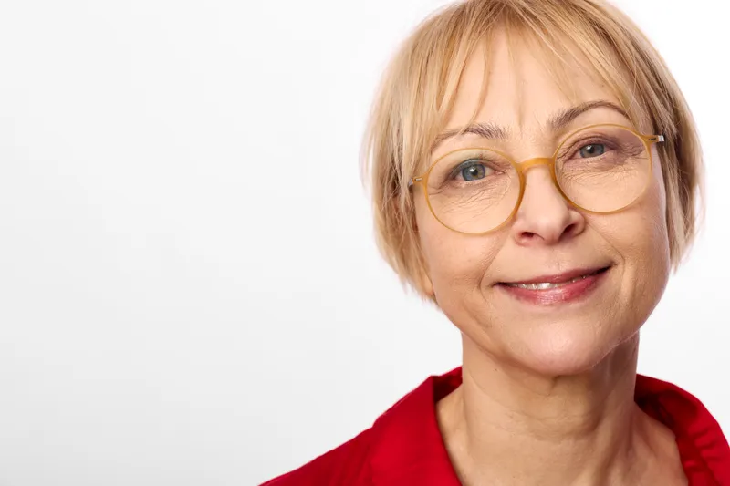 Woman smile portrait, senior blond short hair with glasses, closeup on white background, friendly calm mood, soft studio lighting, headshot view, warm expression