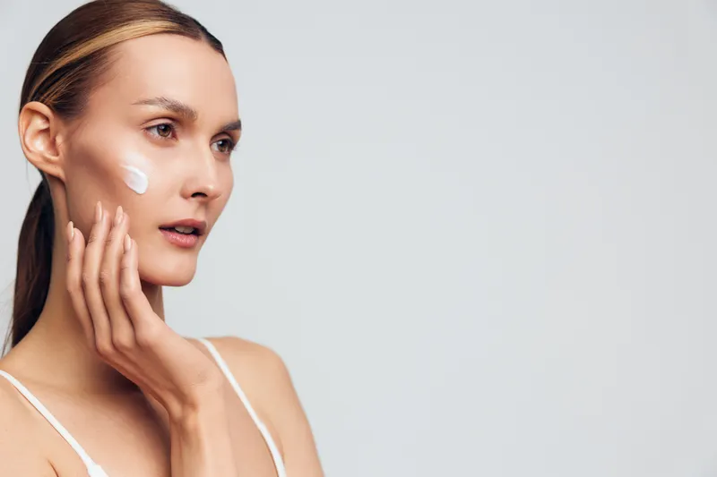 Woman skincare beauty face portrait wellness spa young, model touches her cheek, soft studio daylight, smooth glowing complexion, calm expression, minimal white background