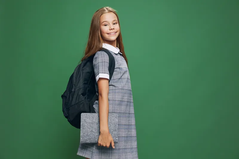Girl, schoolchild and backpack standing with book for education at studio. Young student, smiling child holding notebook in casual dress with long hair on green background for learning concept.