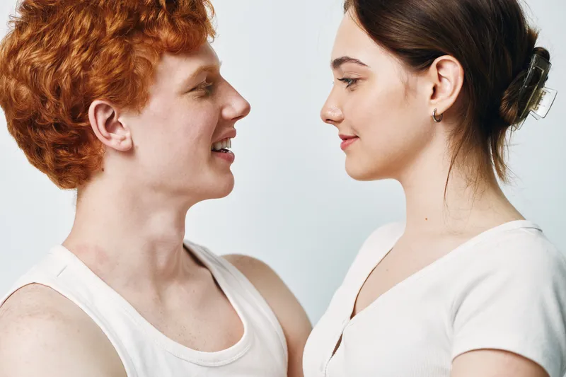 Young man and woman facing each other smiling in casual clothes with natural light against plain background for friendship and communication concept.