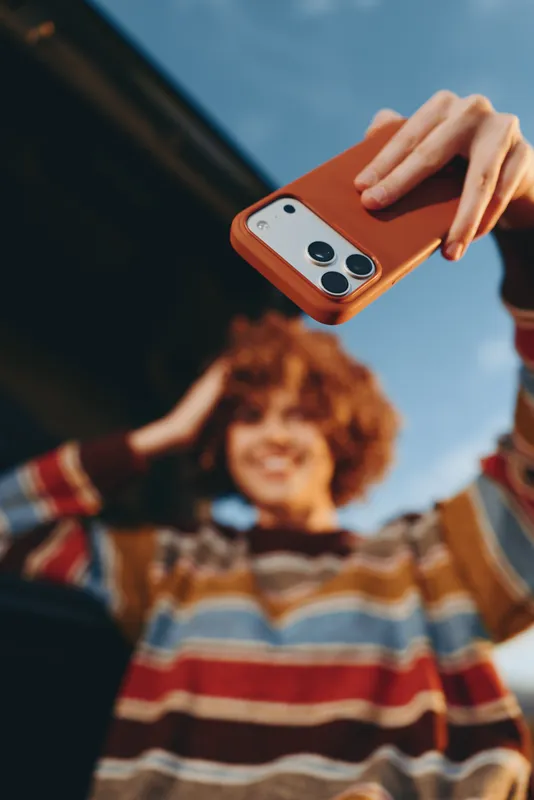 Woman lifestyle scene with smartphone in hand capturing a photo of a smiling child in a family moment outdoors, playful mood, soft daylight, close up portrait with blurred background