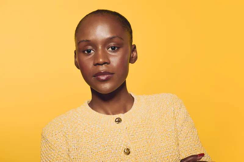 Confident African woman with dark skin wearing a yellow textured sweater stands with arms crossed against a bright yellow background. Concept for empowerment, fashion, and beauty.