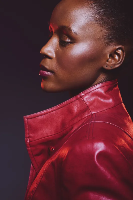 Profile of a dark skinned African woman wearing a red leather jacket. Studio portrait with dramatic lighting highlights smooth skin and confident expression. Fashion and beauty concept.