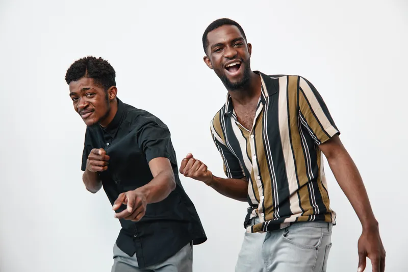 Two young black men with dark skin posing and smiling in casual clothes on white background. Friends having fun, dancing and enjoying positive energy together indoors.
