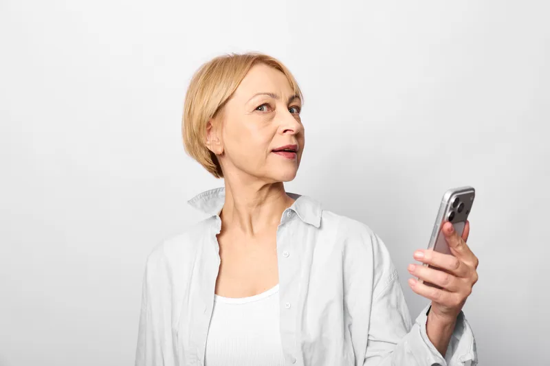 woman senior smartphone portrait indoor communication technology holding thinking thoughtful expression soft studio light neutral white background calm relaxed posture sideways