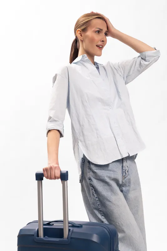 Young woman in casual outfit standing with suitcase, looking away thoughtfully. Concept of travel, lifestyle, and preparation for journey or vacation.
