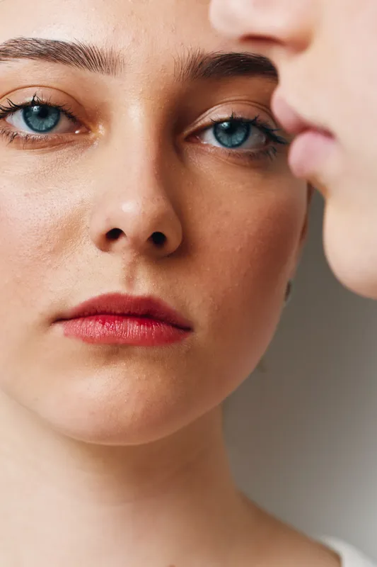 Closeup of two young women with blue eyes and natural skin, showing facial features, lips, and eyebrow details for beauty and portrait photography concept.
