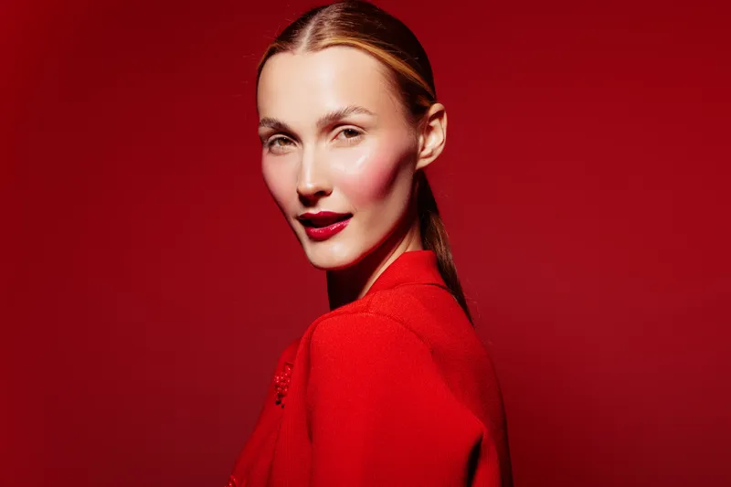Portrait of confident woman with red lipstick and sleek hair wearing red sweater on red background. Concept of fashion, beauty, elegance, and style in studio lighting.