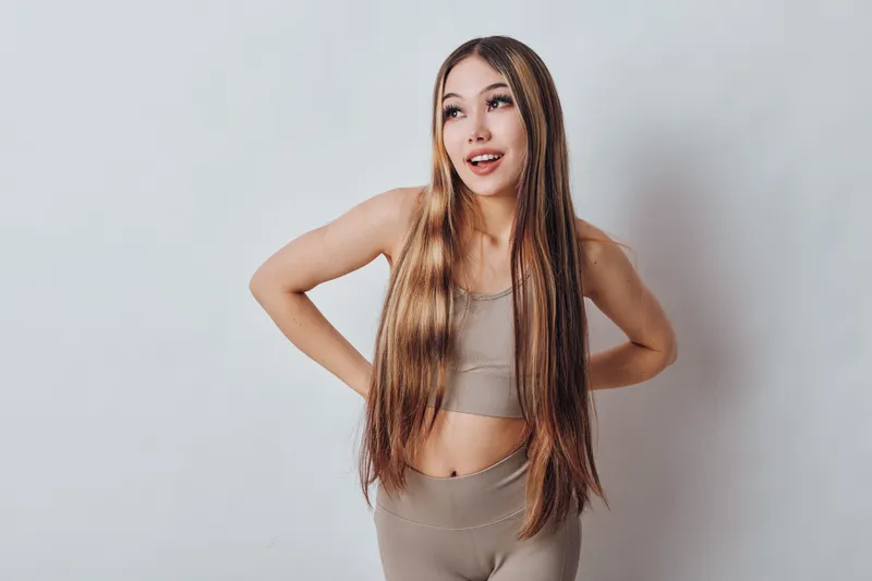 Young woman posing with long braided hair and casual outfit standing against plain background looking sideways with smile and relaxed posture for lifestyle concept.