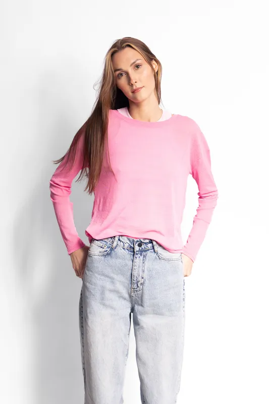 Young woman with long hair wearing pink sweater and light blue jeans stands against white background with hands in pockets. Casual fashion and style concept for everyday wear.