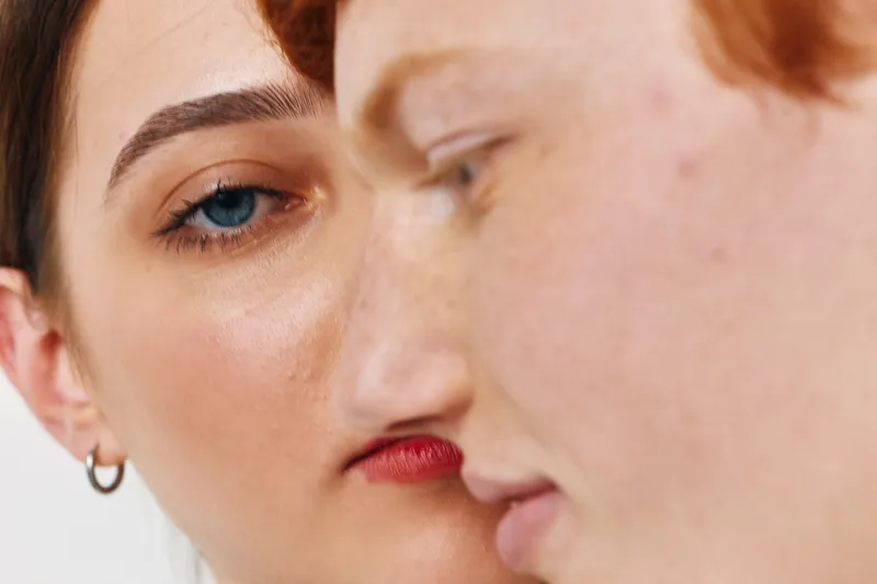 Closeup of two young people facing each other with serious expressions, showing skin texture and natural features, focused on eyes and lips in portrait style.