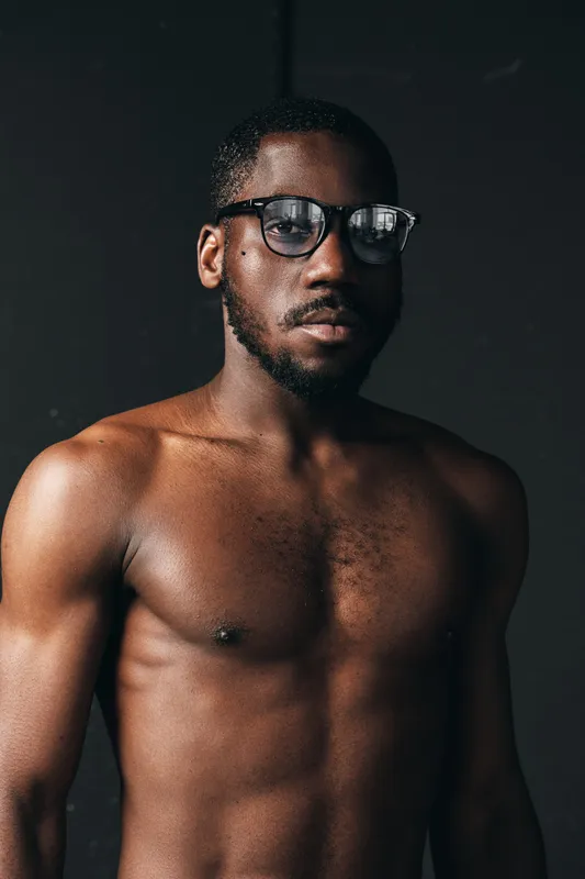 African man with glasses and bare chest in creative conceptual visual style, portrait with serious expression and dark background for artistic photography series.