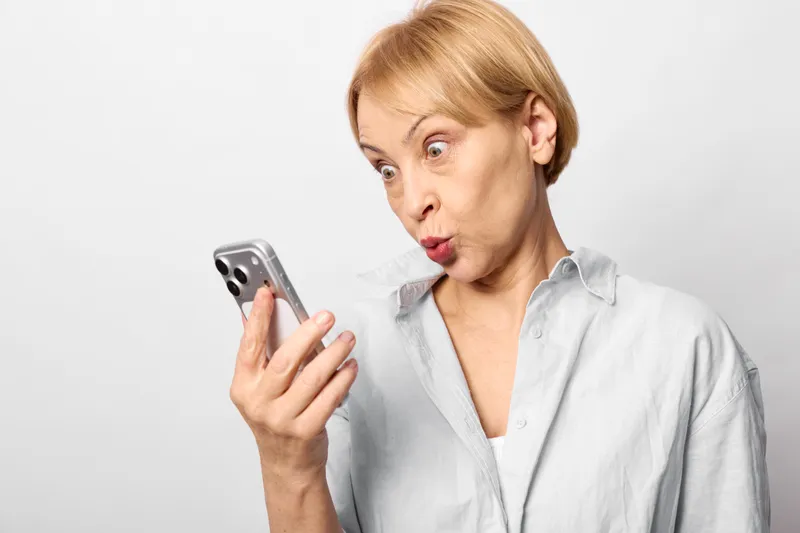 Woman holding smartphone with surprised expression, using technology for communication, studio portrait on white background, expressive face gesture, everyday emotion closeup