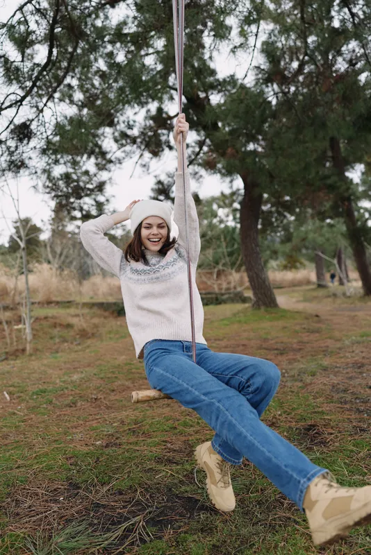 joyful swing scene in outdoor park, girl in casual clothing smiles as she swings, graceful playful moment among trees and open space, fresh air and sunlight, candid outdoor leisure