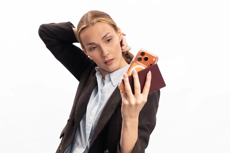 Young woman in brown jacket takes selfie with smartphone, posing with hand behind head. Isolated on white background. Concept of social media, communication, and modern lifestyle.