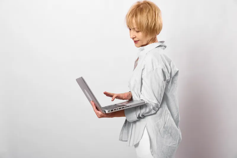 Woman laptop office technology professional white coat remote work education in studio, side view of calm business woman holding open laptop, using keyboard for online tasks, plain background