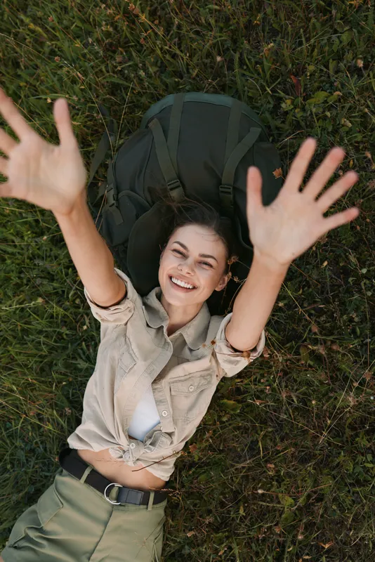 Woman lifestyle outdoor scene lying on grass with backpack, smiling, carefree, casual in a relaxed pose under sunny weather, capturing a joyful moment of freedom and travel