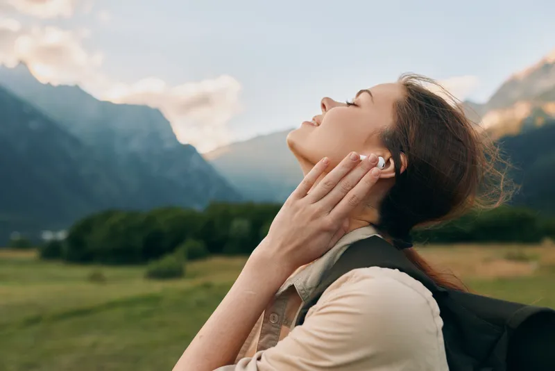 A woman enjoys the outdoors in a mountain landscape, head tilted back to feel the breeze in bright open air. A serene moment of nature, calm and breathing freely.
