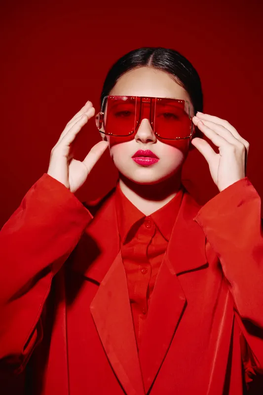 Fashionable young woman in oversized red sunglasses and a matching red blazer poses against a red background. Bold beauty and style concept with chic color blocking and attitude.