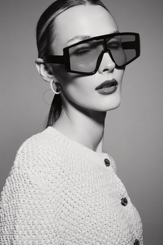 Stylish white woman with pale skin wears large black sunglasses and white knitted top. Studio portrait in black and white with elegant fashion concept.