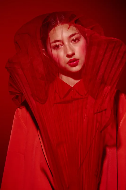 Portrait of a young woman in avant-garde red fashion with bold lipstick and dramatic red mesh lighting, creating a creative, artistic beauty and fashion concept.