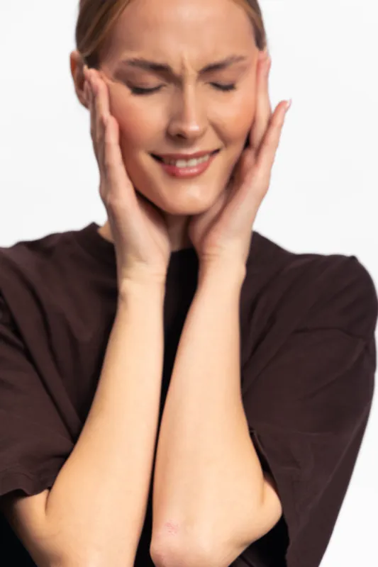 Young woman with closed eyes holds hands to her face, expressing pain or discomfort. Isolated on white background. Concept of headache, stress, and emotional distress.