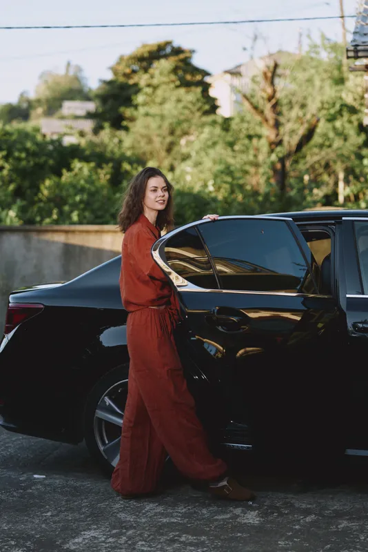 Woman in red outfit standing beside a sleek car outdoors, capturing lifestyle and fashion with a confident, relaxed mood and bright daylight