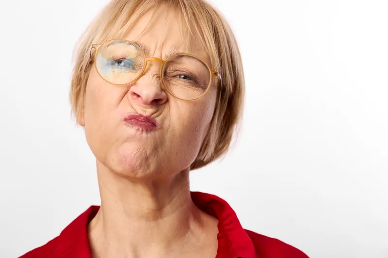 Playful woman portrait in studio, wearing glasses and red shirt, face paint on cheeks and lips, looking at camera with quirky expression, white background