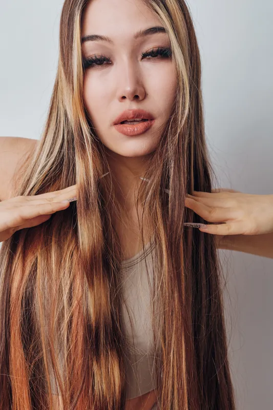 Young woman with long straight hair posing with hand near head, natural makeup and neutral background for beauty, fashion and hairstyle concept portrait studio.
