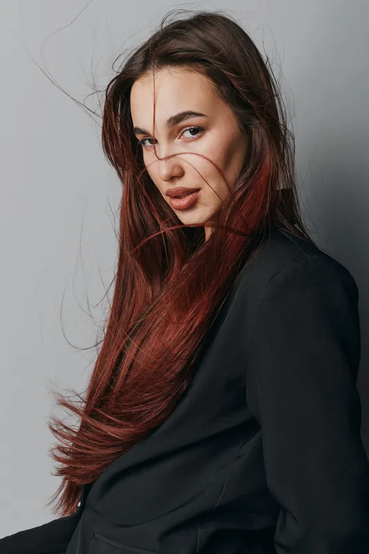 Portrait of woman with long red hair wearing black jacket looking at camera with serious expression, studio background and natural makeup for fashion and beauty concept.