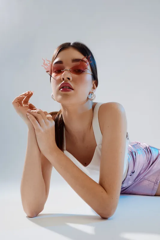 Fashionable young woman wearing pink sunglasses and a white top poses confidently against a light background. Concept for beauty, fashion, and modern style.