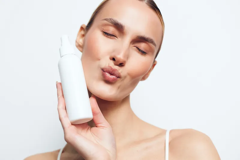Woman in close up holding skincare bottle, eyes closed, facial serum application, beauty hydration routine on calm neutral background, concept of self care and skincare