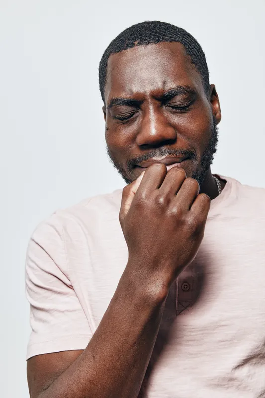 African American man with dark skin wearing light pink shirt biting nails and showing anxiety or nervousness isolated on white background. Closeup, stress and worry expression on face.